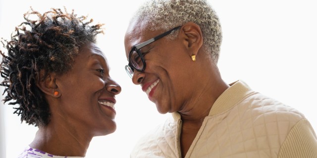 Two older black lesbians with short grey hair stare at each other lovingly.