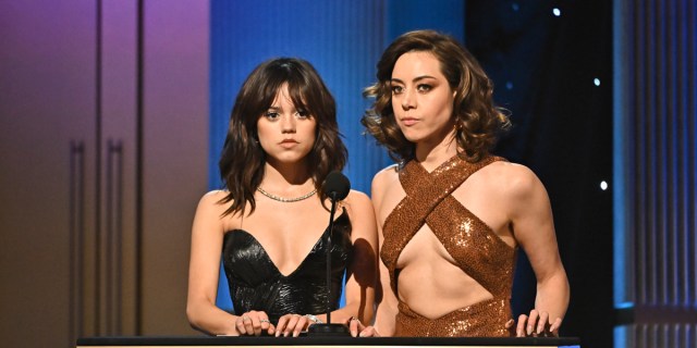 Aubrey Plaza and Jenny Ortega make deadpan faces on stage at the Screen Actors Guild Awards. Aubrey's in a bronze dress that also exposes her midriff.