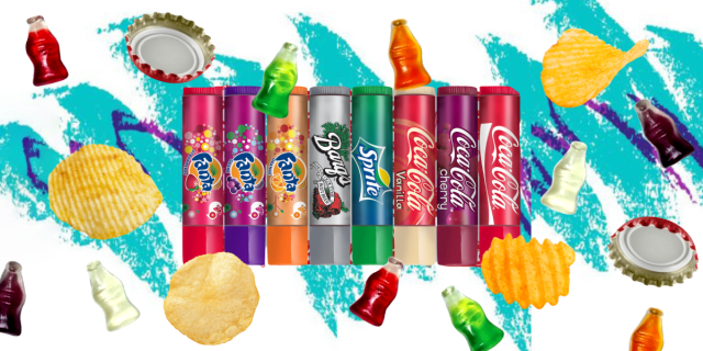 Lip Smacker chapsticks in fanta strawberry, fanta grape, fanta orange, root beer, sprite, coca-cola vanilla, cherry coke, and coca-cola classic, surrounded by gummy sodas, potato chips, and bottle caps.