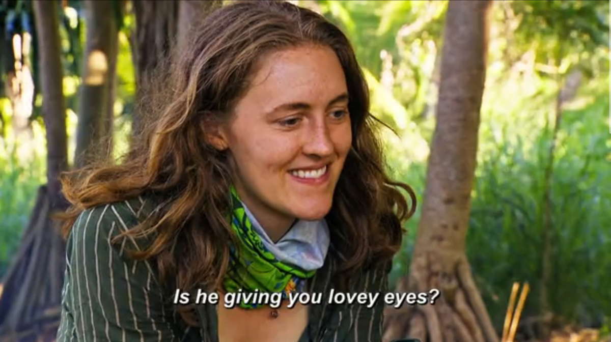 Survivor 44 contestant Frannie Marie smiles while looking off camera, listening as someone asks her "Is he giving you lovey eyes?"