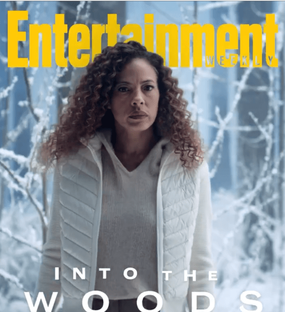the entertainment cover with tawny cypress, a tall Black woman with long hari, standing in winter clothes in the woods
