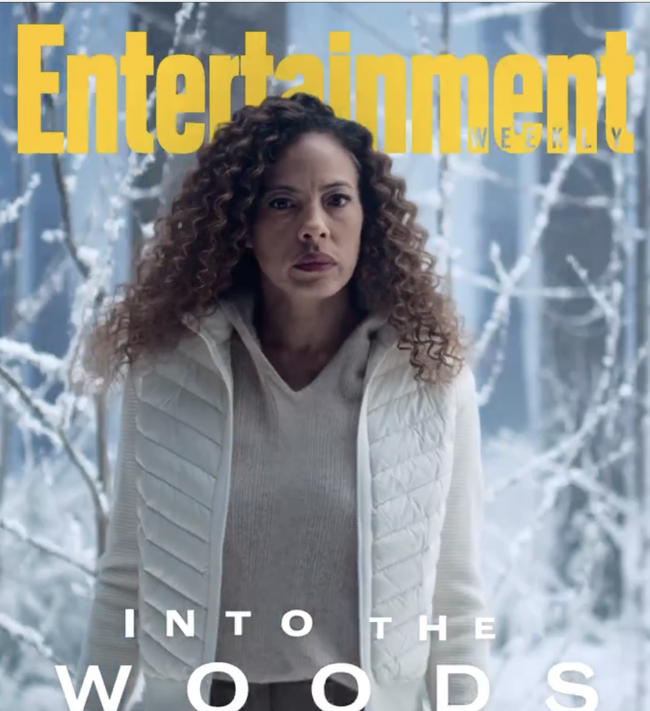 the entertainment cover with tawny cypress, a tall Black woman with long hari, standing in winter clothes in the woods