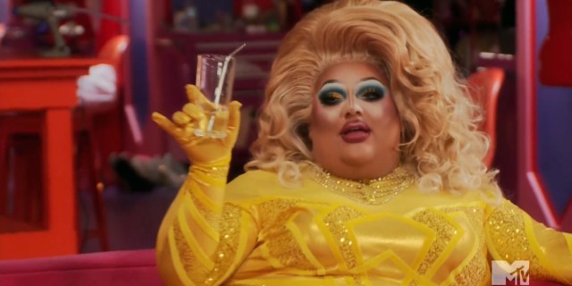 Mistress in a yellow gown with connected yellow gloves lifts up a glass to toast during Untucked.