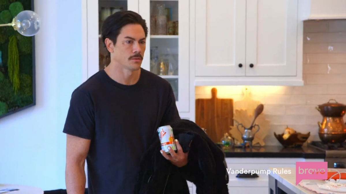 a white man with brown hair and a mustache wears a black tee and holds a can of diet squirt