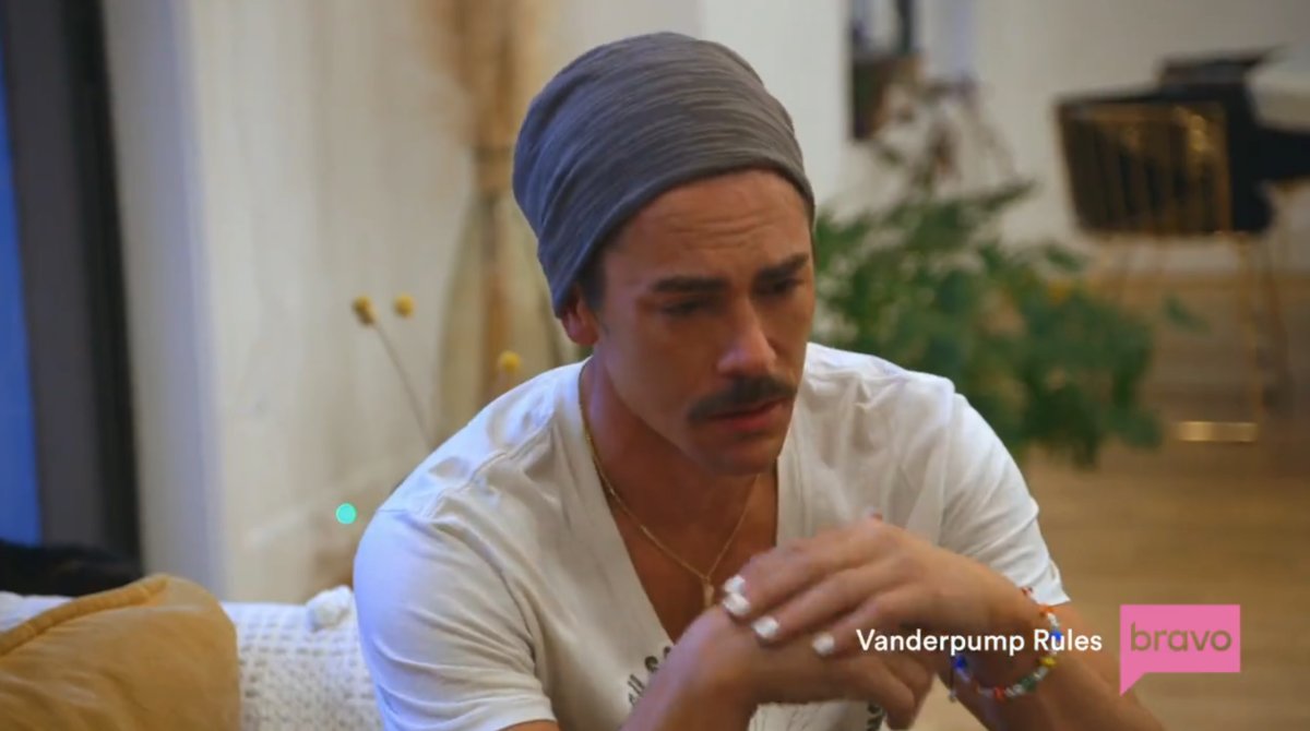 a white man wearing a gray beanie with a mustache and white painted fingernails cries