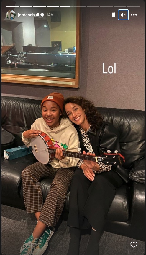 Jennifer Beals and Jordan Hull sitting on a couch together with a banjo