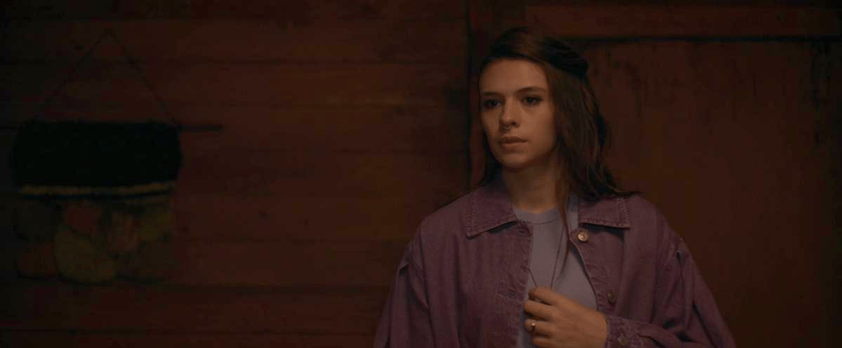 Natalie Maines in Yellowjackeets 201 wears purple and has her hand on her chest