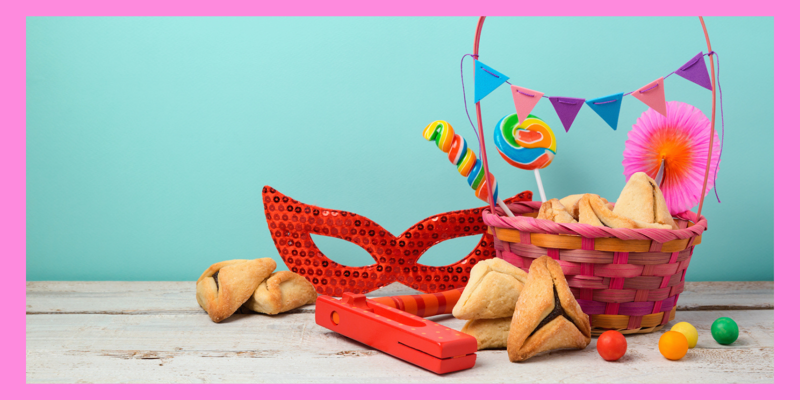A pink frame surrounds a photo of a mishloach manot, a gift basket specifically given to friends on Purim. The basket contains hamentaschen, a mask, noise makers, and other treats.