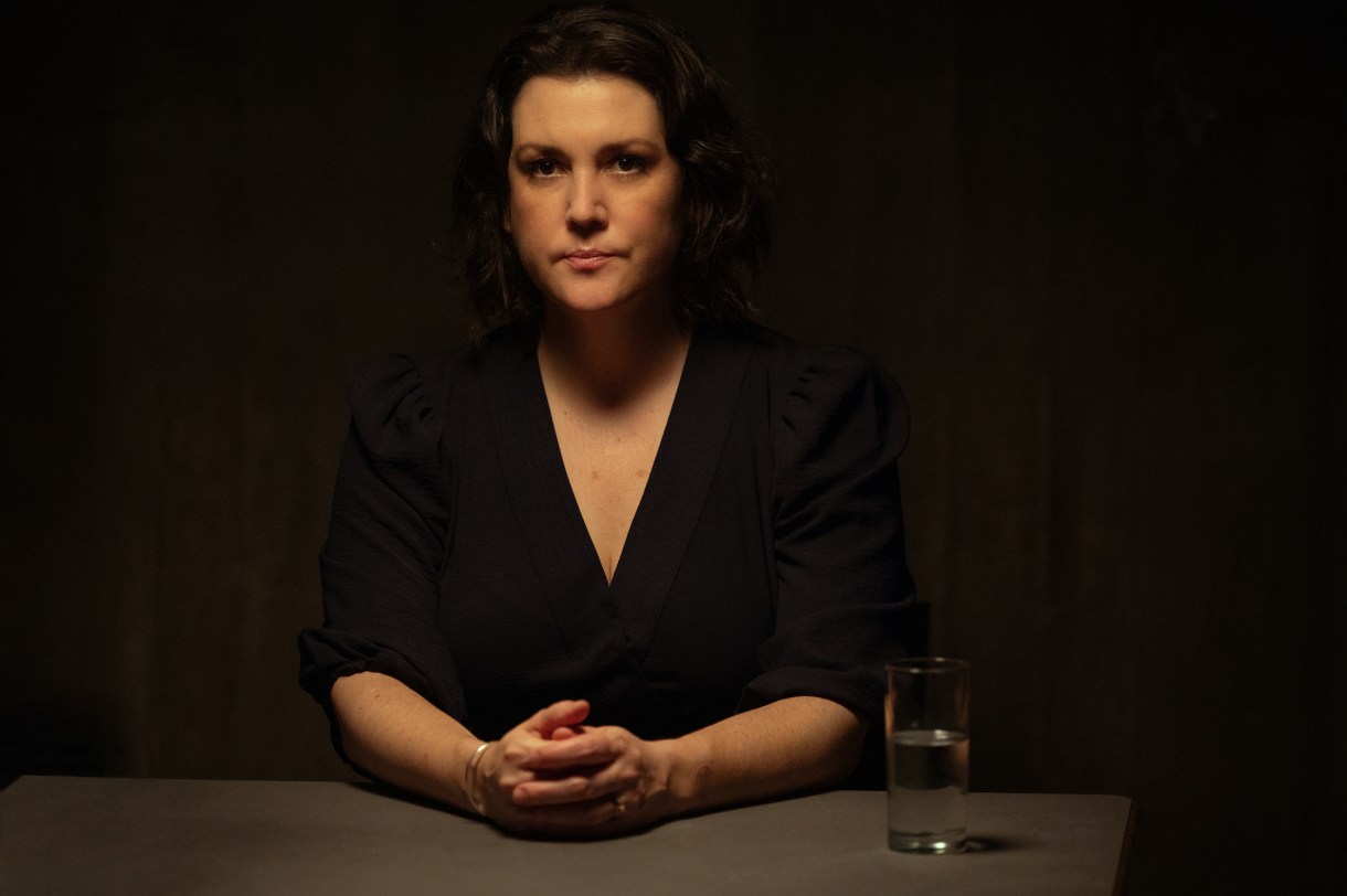 Melanie Lynskey as Shauna in YELLOWJACKETS sits at a table and faces the camera. Season 2. Photo Credit: Kimberley French/SHOWTIME.