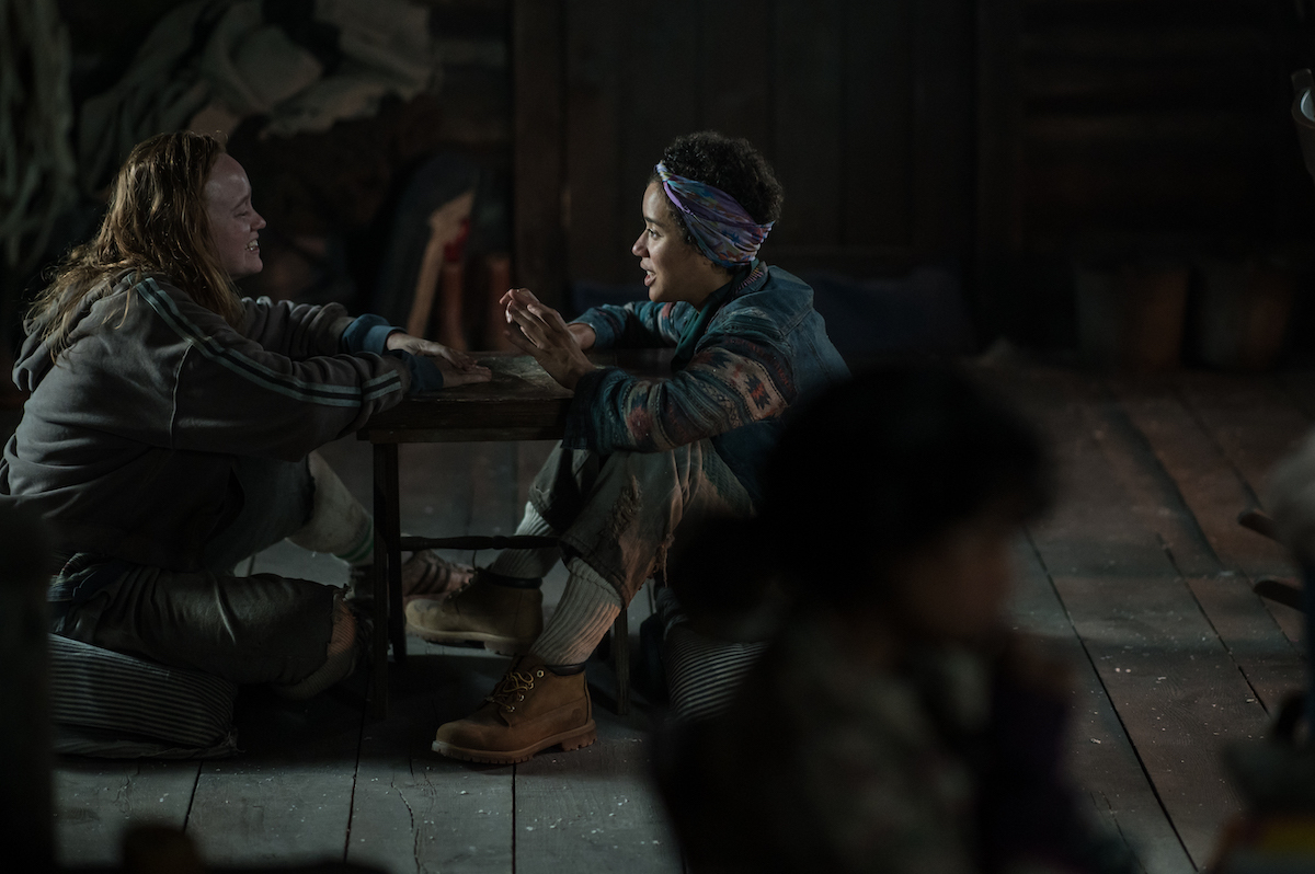 (L-R): Liv Hewson as Teen Van and Jasmin Savoy Brown as Teen Taissa in YELLOWJACKETS Season 2 sitting on the floor holding their hands up. Photo Credit: Kailey Schwerman/SHOWTIME.