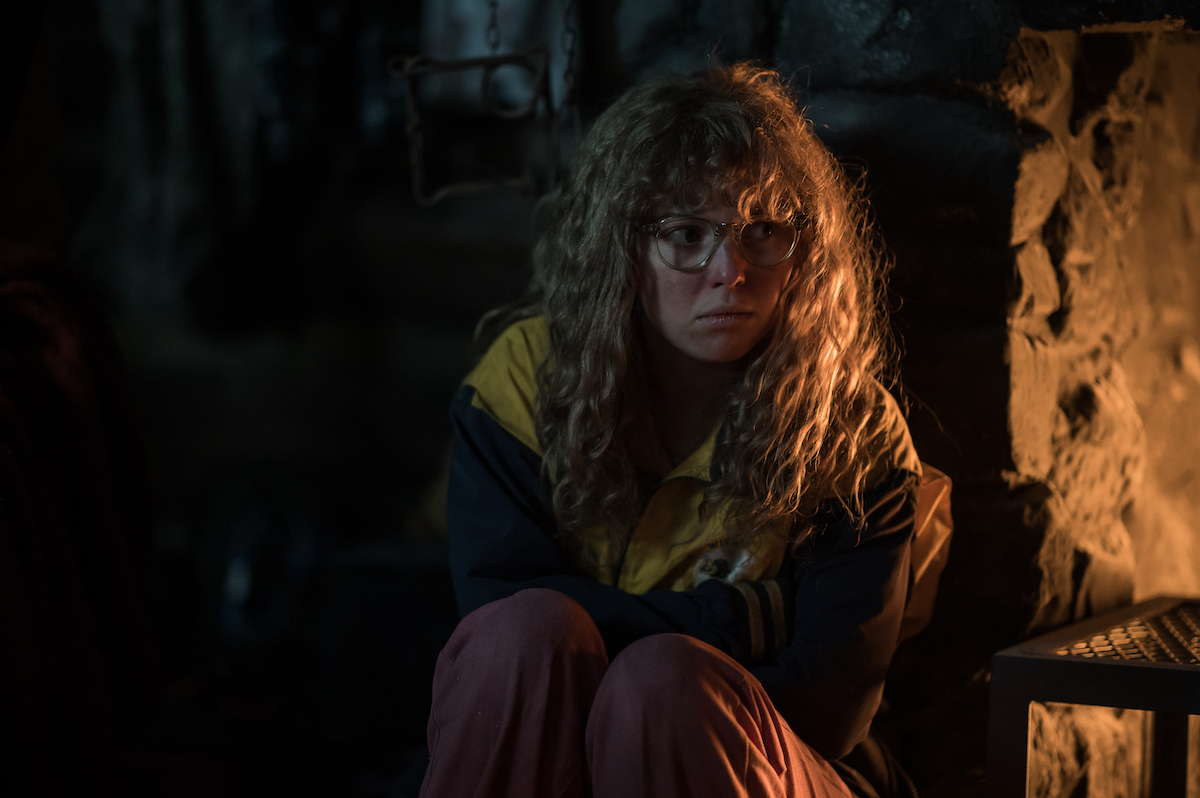Samantha Hanratty as Teen Misty in YELLOWJACKETS Season 2 kneels in a dark corner. Photo Credit: Kailey Schwerman/SHOWTIME.