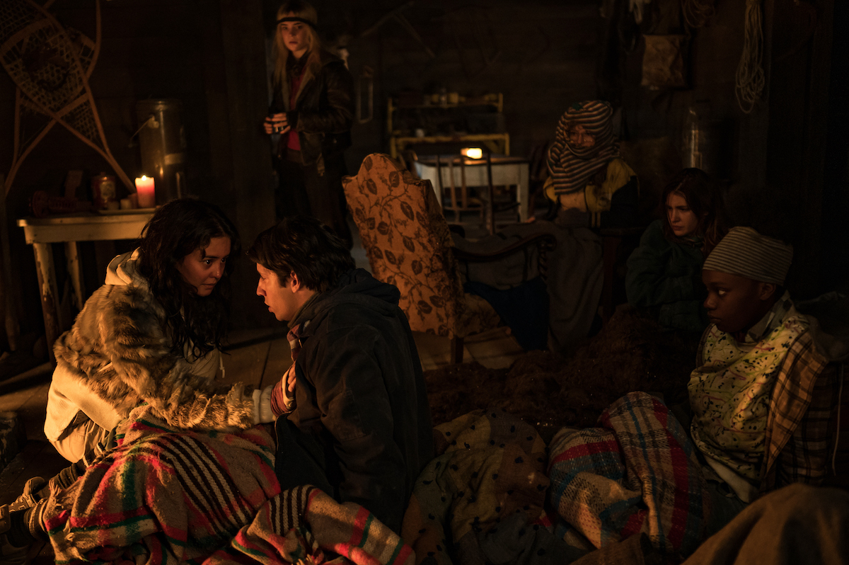(L-R): Courtney Eaton as Teen Lottie, Kevin Alves as Teen Travis, Sophie Thatcher as Teen Natalie, Samantha Hanratty as Teen Misty, Sophie Nélisse as Teen Shauna and Nia Sondaya as Teen Akilah in YELLOWJACKETS Season 2 sit in a cabin glowing in fire light. Photo Credit: Kailey Schwerman/SHOWTIME.