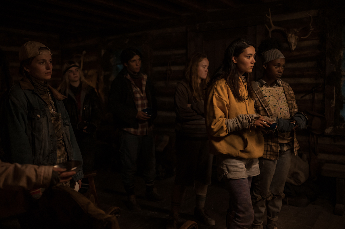 (L-R): Jenna Burgess as Teen Melissa, Sophie Thatcher as Teen Natalie, Kevin Alves as Teen Travis, Liv Hewson as Teen Van, Alexa Barajas as Teen Mari and Nia Sondaya as Teen Akilah in YELLOWJACKETS Season 2 stand in a group in the cabin. Photo Credit: Kailey Schwerman/SHOWTIME.