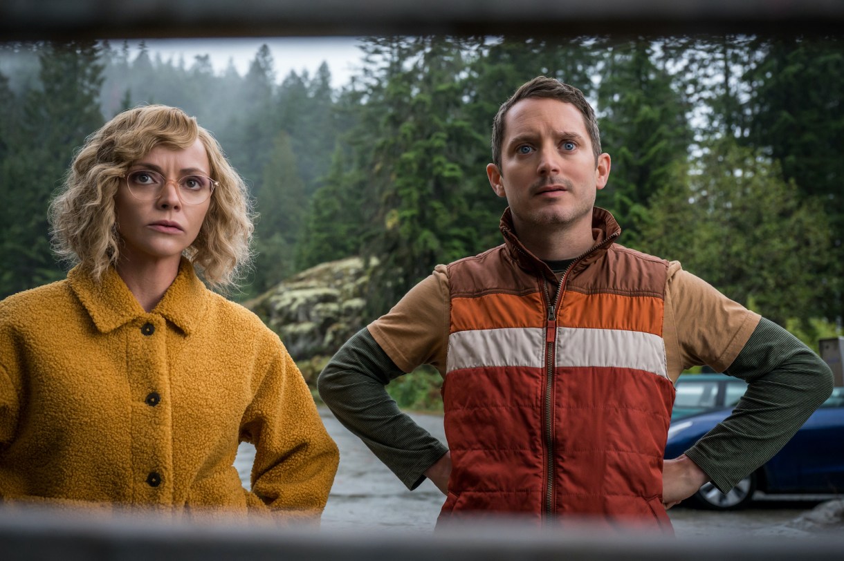 (L-R): Christina Ricci as Misty and Elijah Wood as Walter in YELLOWJACKETS Season 2 stand looking at something in the woods. Photo Credit: Kailey Schwerman/SHOWTIME.