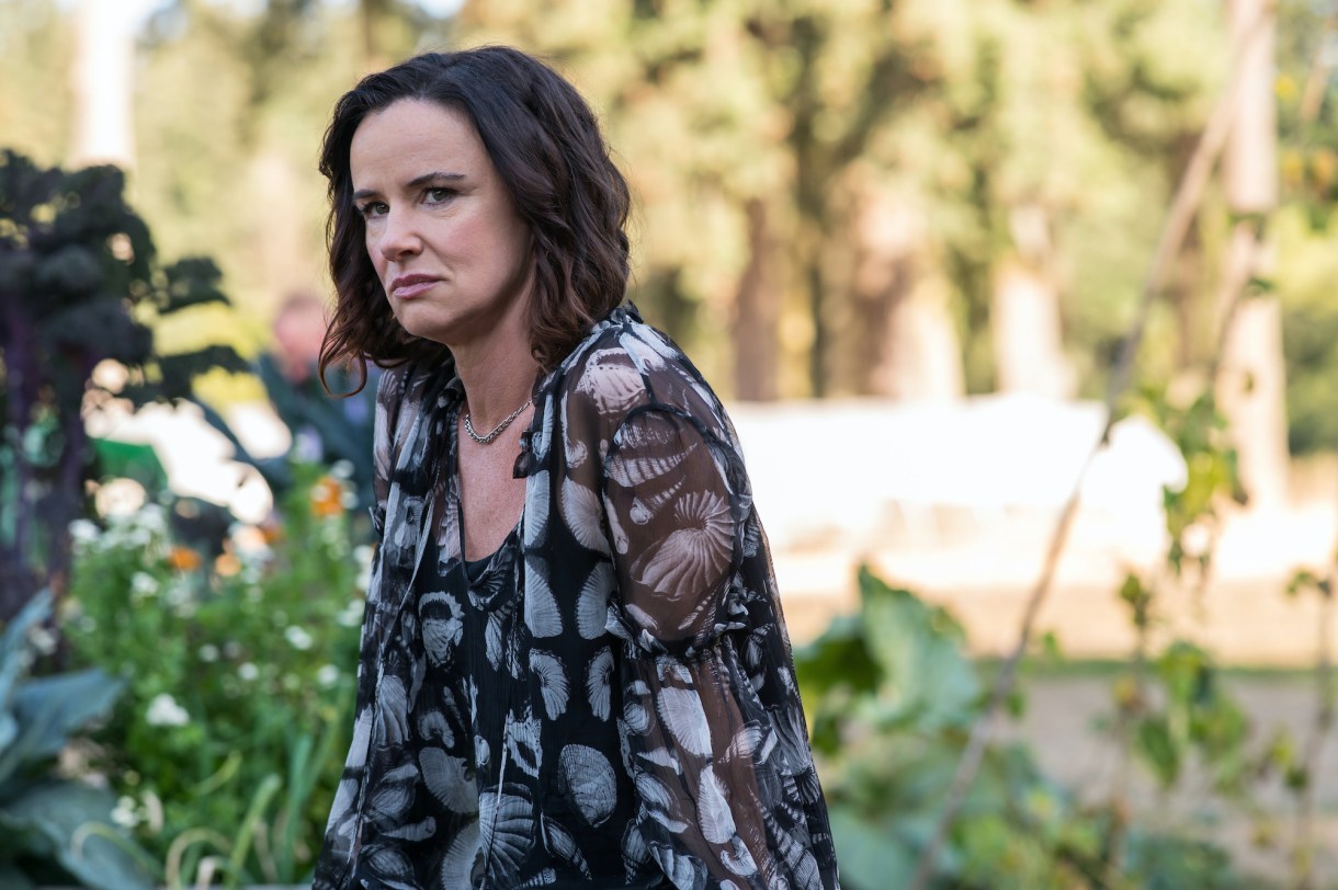 Juliette Lewis as Natalie in YELLOWJACKETS S2 sits in a garden in a floral dress. Photo Credit: Kailey Schwerman/SHOWTIME.