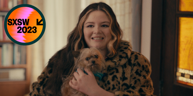 A still from the film "Cora Bora" with the SXSW 2023 logo in the left corner. She is wearing a leopard jacket, holding a dog, and has an awkward look on her face.