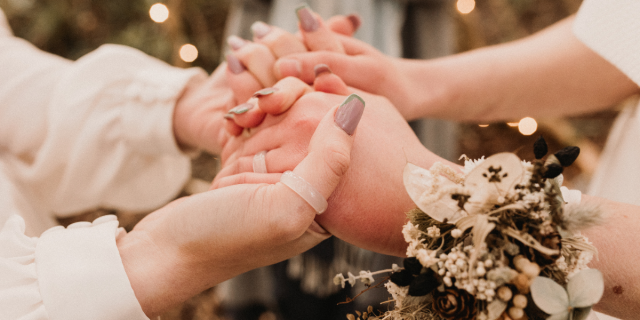 two corsaged sets of hands hold each other in close up during a lesbian wedding.