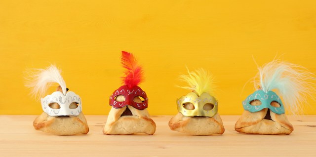 Four hamentaschen cookies are dressed up in masks and costumes against a yellow background. Very silly and very cute.