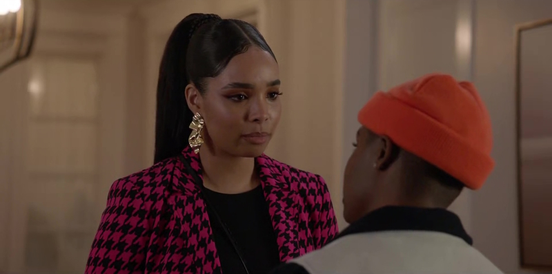 Skye laments Coop's broken promises and decides to end their relationship. Coop's in the foreground of the shot, with her back to the audience, wearing a two-tone jacket and orange beanie. Skye is standing in front of her, wearing ornate earrings, a black shirt and pink and black checkered blazer.