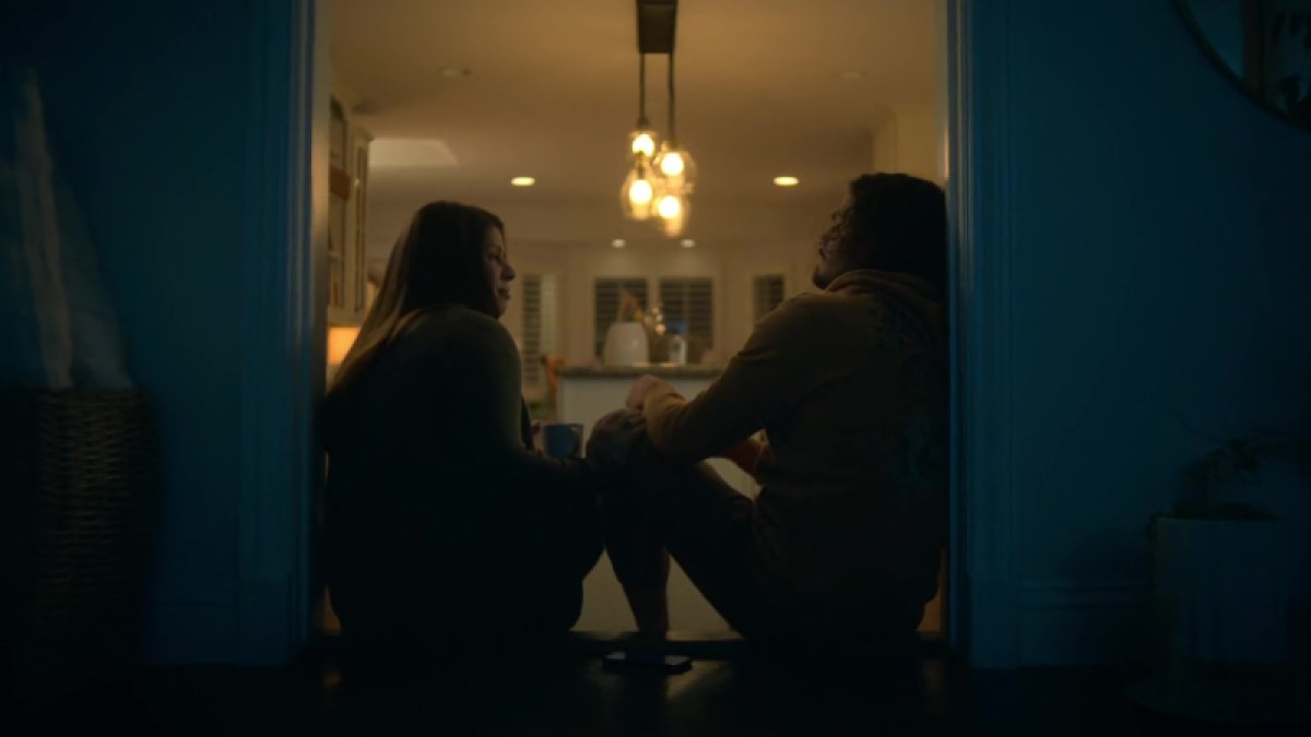 Jazmin and Gael share a cup of tea in the kitchen doorway. Gael is on the left, in a yellow hoodie and linen pants. Jazmin is on the right, wearing an oversized sweater (classic Mommi gear). 
