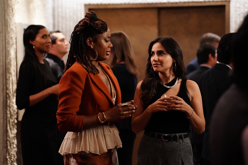 Malika (L) and Angelica (R), both holding drinks, glance at each other as they try to come up with a plan to approach the councilman.