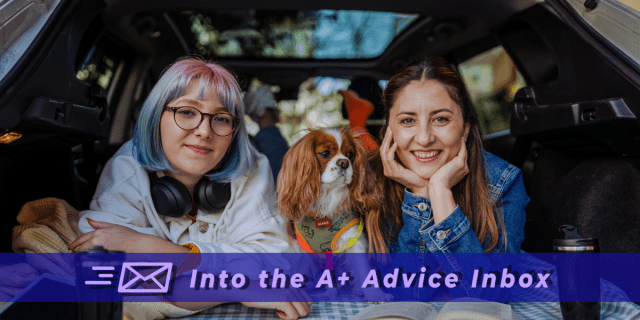 A photo of a happy queer family posed in the back of their hatchback with a small, cute dog while traveling or road tripping while gay. One is a white person with a multi-colored banged bob. Another is a white person with long brown hair.