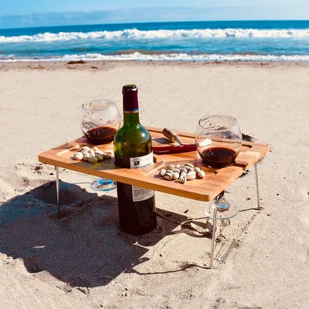 a portable picnic table by the beach with two wine glasses and a wine bottle in it