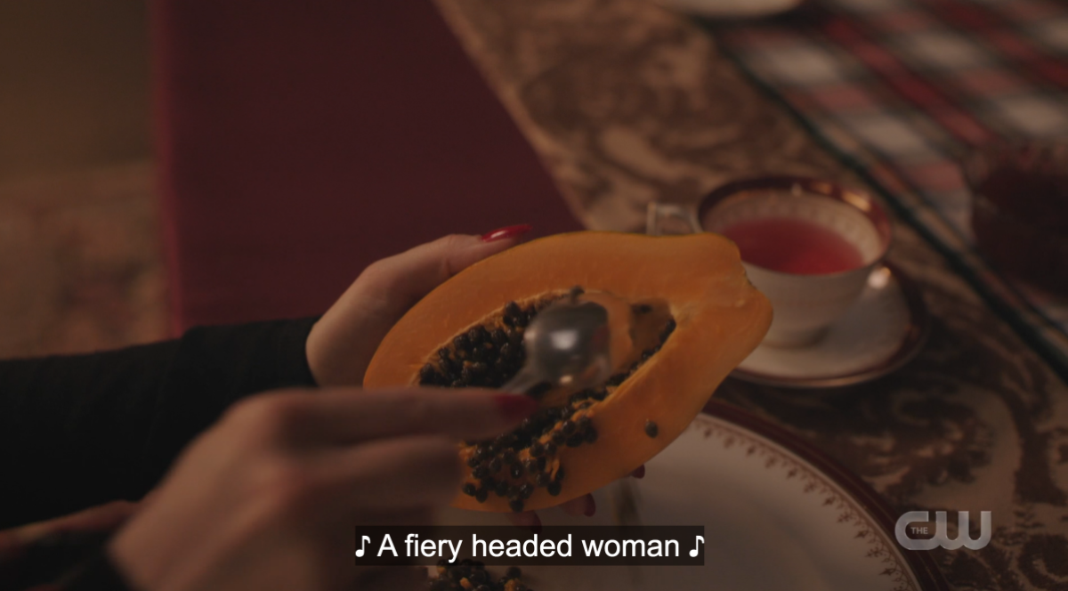Cheryl scoops out papaya while "a fiery headed woman" is sung over top it