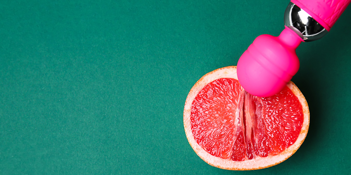 Against a teal background, half of a grapefruit is in the bottom right corner of the image. A hot pink wand vibrator extends from the upper right corner and rests against the grapefruit.