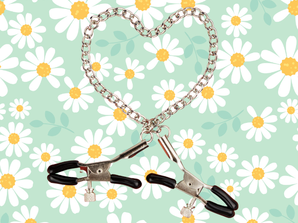 Against a light green background covered in drawings of daisies, black adjustable nipple clamps for intense nipple stimulation are on a silver chain form the shape of a heart.