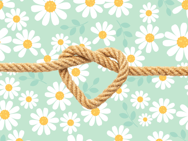 Against a light green background covered in drawings of daisies, there beige rope tied in the shape of a heart.