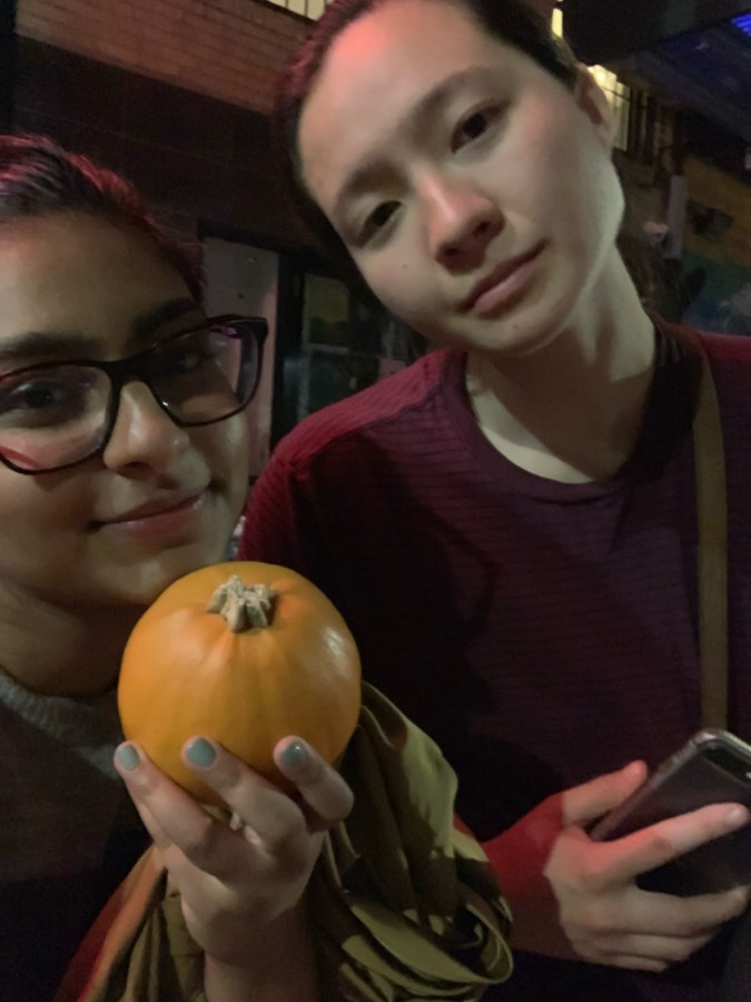 Ashni (left) is holding a baby pumpkin. MR (right) is wearing a red sweater.