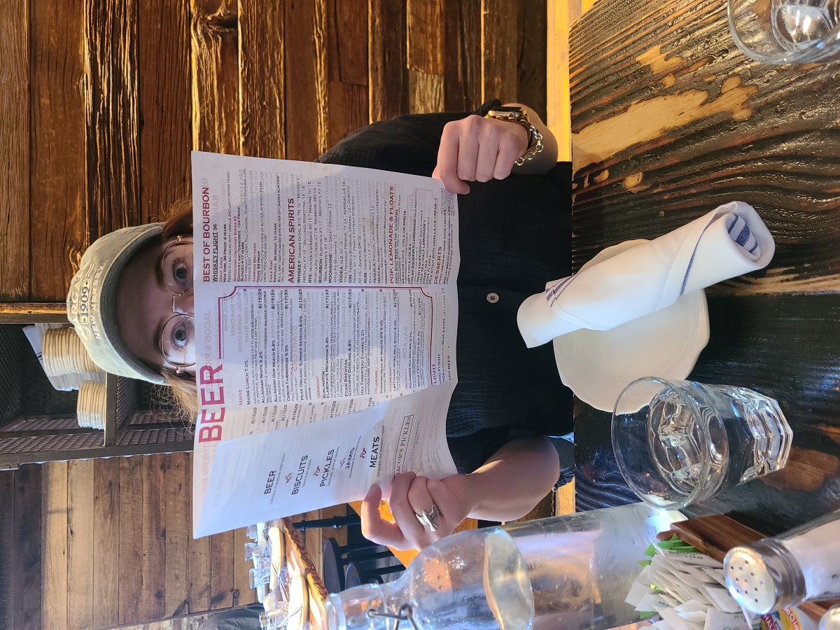 Jess, a white woman with glasses and a baseball cap, holds a menu at Jacob's Pickles