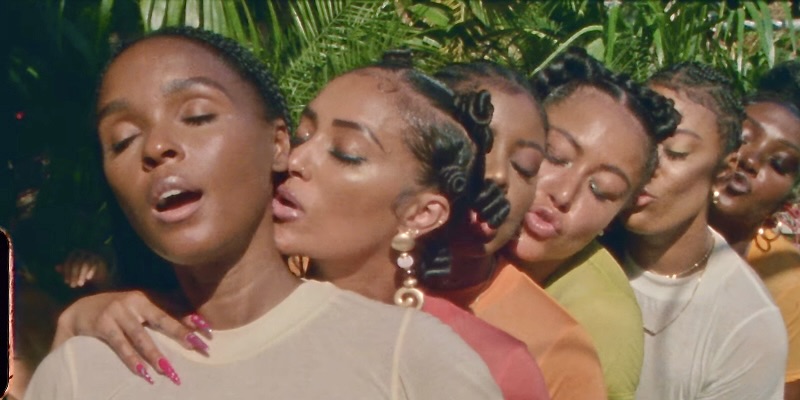 In a still from Janelle Monae's Lipstick Lover music video, a group of Black women line up to kiss each other underneath the sunlight in their bathing suits.