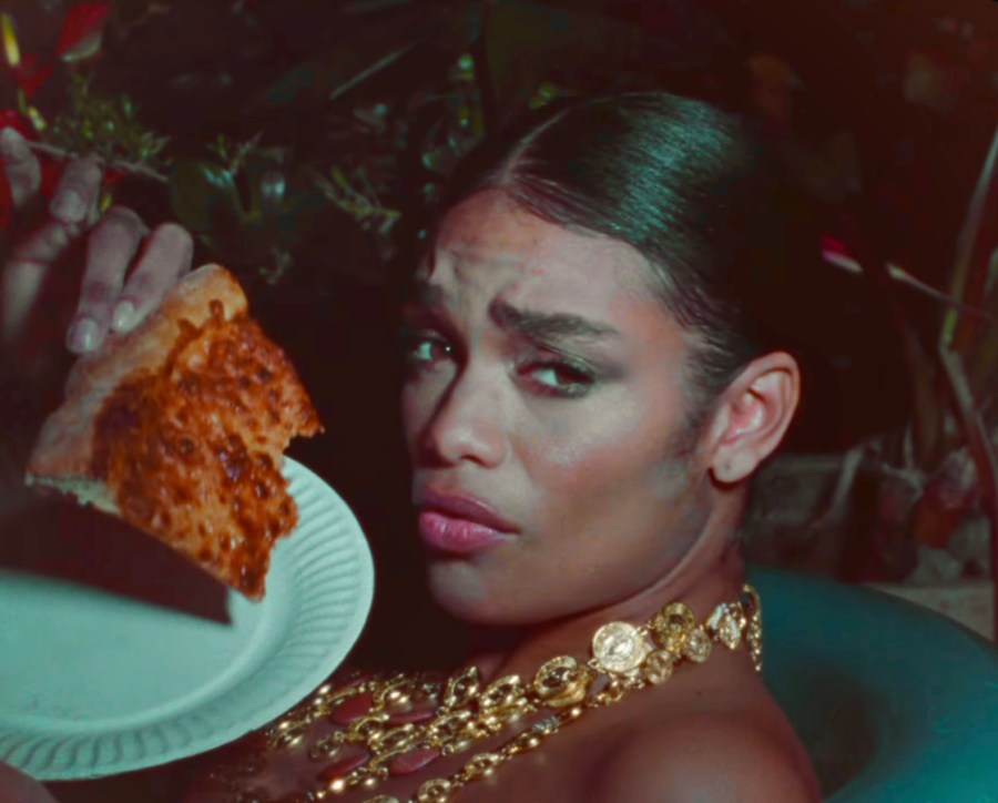 In a still from Janelle Monae's Lipstick Lover music video, someone eats a piece of pizza while in a pool.