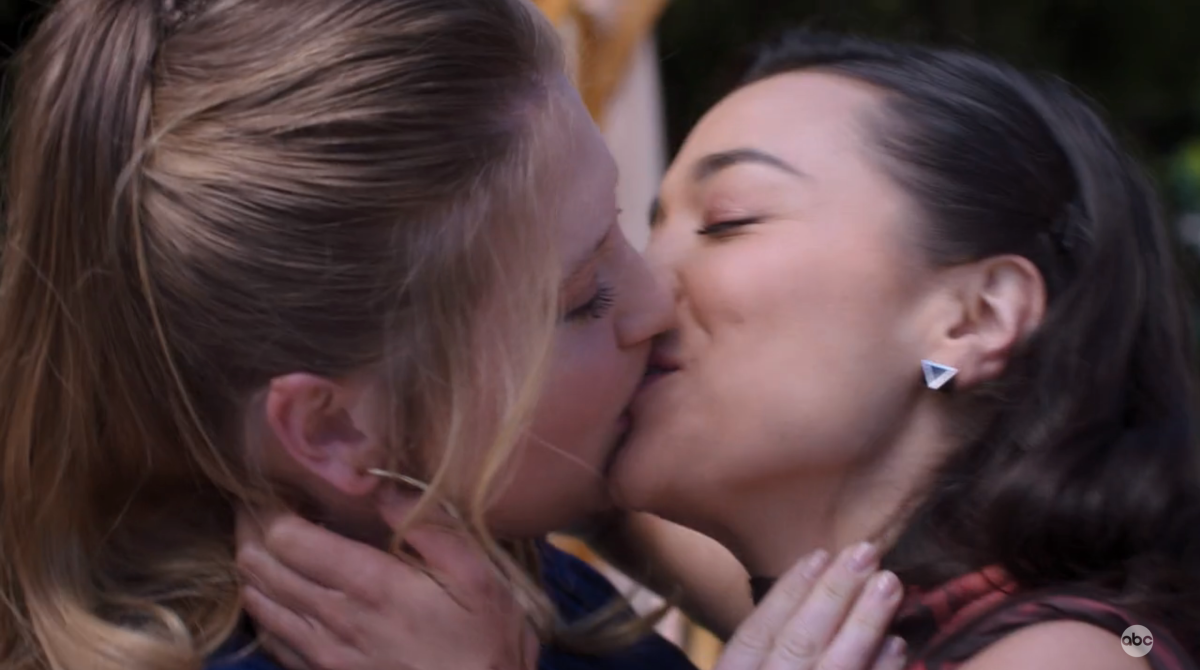Taryn Helm and Mika Yasuda kiss outside at a wedding.