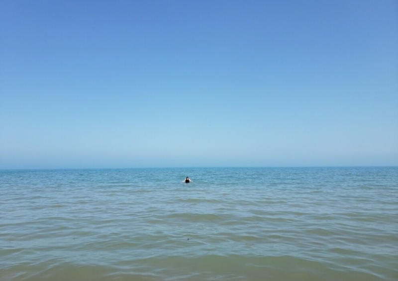 A tiny speck of a person in a huge blue lake, with blue water above them