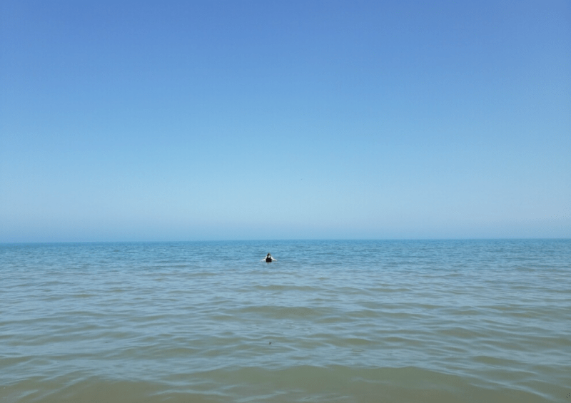 A tiny speck of a person in a huge blue lake, with blue water above them