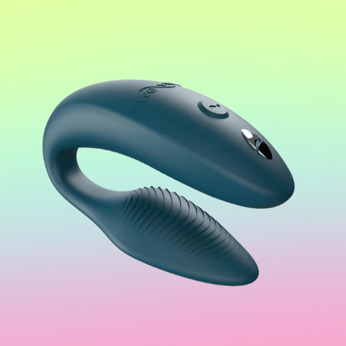 Against a green, blue, and pink ombre background, there is the We-Vibe Sync 2, a C-shaped, teal, silicone vibrator with a button on top. The internal portion has ridges.