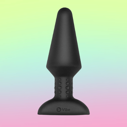 Against a green, blue, and pink ombre background, there is the B-Vibe Rimming. Plug, a black, silicone butt plug with a long, wide step. The internal portion is cone-shaped.