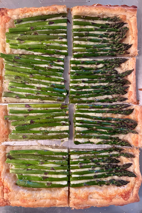 A four-ingredient asparagus tart, in a close up photo. Asparagus spears are sitting in a cheese and puff pastry shell.