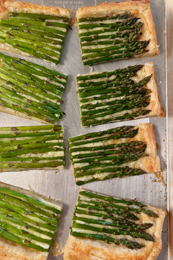 A four-ingredient asparagus tart, cut into pieces in a close up photo. Asparagus spears are sitting in a cheese and puff pastry shell.