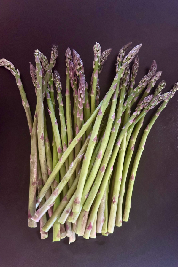 A bundle of asparagus laid on top of a black table top
