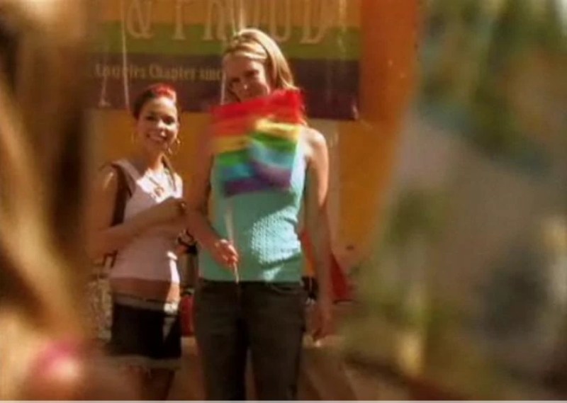a blonde white woman holds a Pride flag