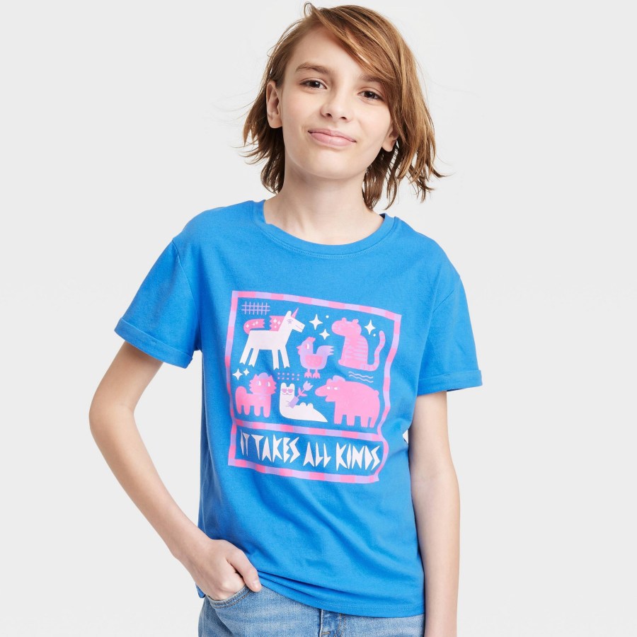 A blue kids shirt that reads "it takes all kinds" along with a variety of mythical creatures in the colors of the trans pride flag