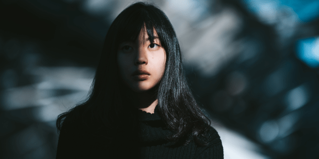 a young East Asian woman with bangs has her face shrouded in shadow