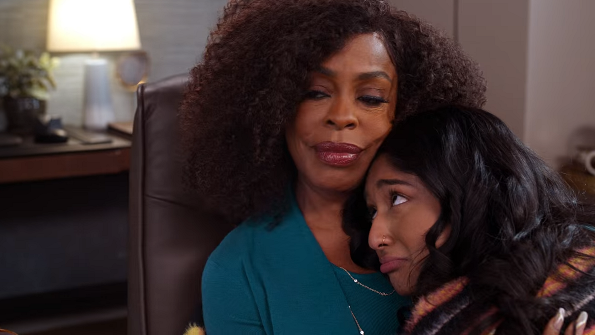 Devi hugs Dr. Ryan (played by Niecy Nash). Looking fabulous as always, Niecy is looking away and smiling, while wearing a teal top with a set of silver chain necklaces. Devi is pouting and looking up at Dr. Ryan.