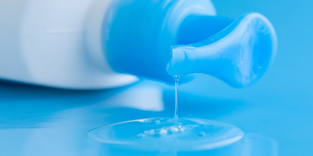 A white plastic lube bottle with a blue pump is on its size on a blue surface. Lube leaks out of the opening.