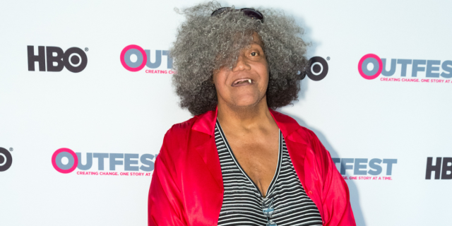 Miss Major on the red carpet for Outfest wearing a black and white striped v-neck and red silk blouse