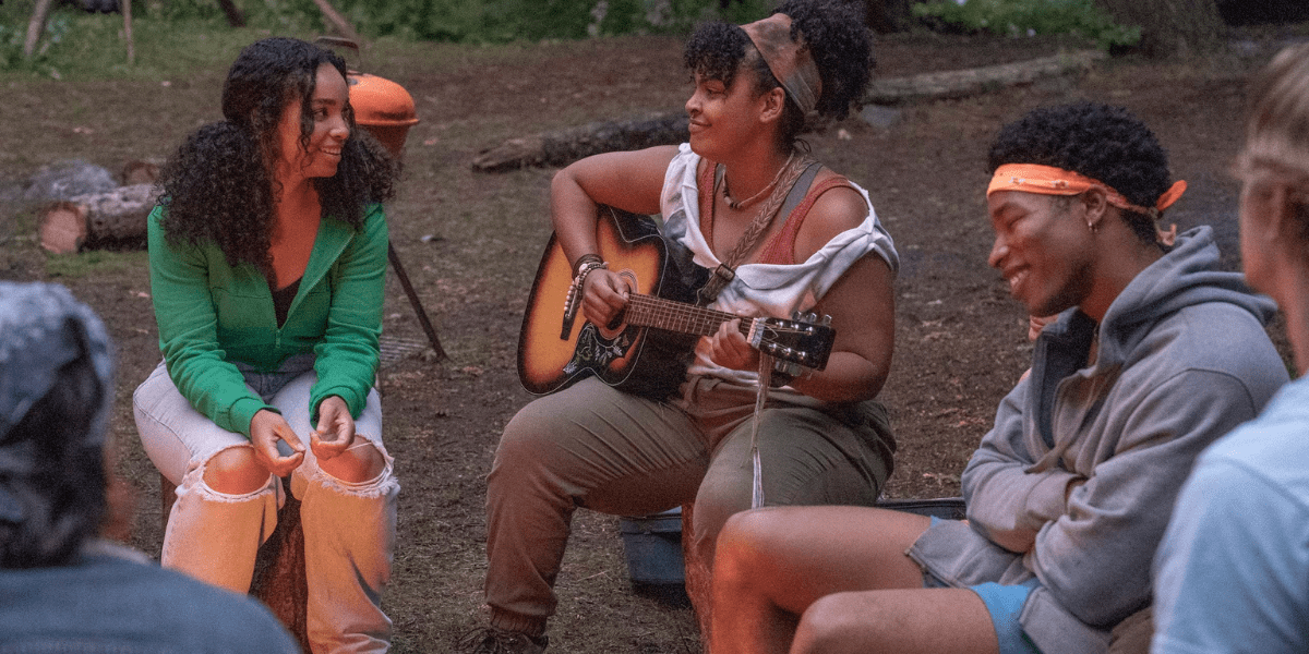 Billie and Ivy sit in a circle in The Lake season two, with Ivy strumming a guitar.